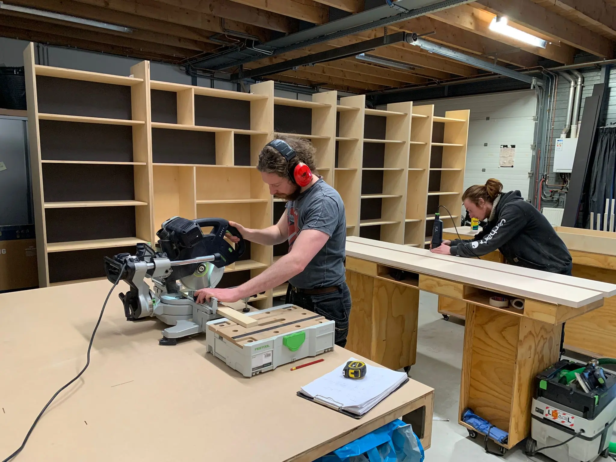 Carpenters working in a workshop. Custom bookshelves in background